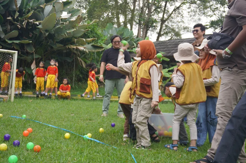 Anak-anak TK bermain lempar bola warna di lapangan rumput
