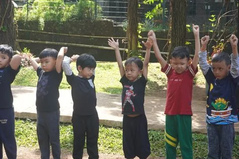 Murid TK mengangkat tangan bersama pendamping di kegiatan alam terbuka